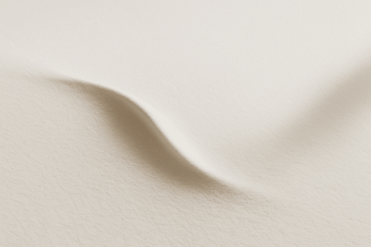 Texture minimaliste en tons beige doux, montrant une légère ondulation dans une surface sableuse ou soyeuse, évoquant la trace d’un souvenir dans une composition paisible et poétique.